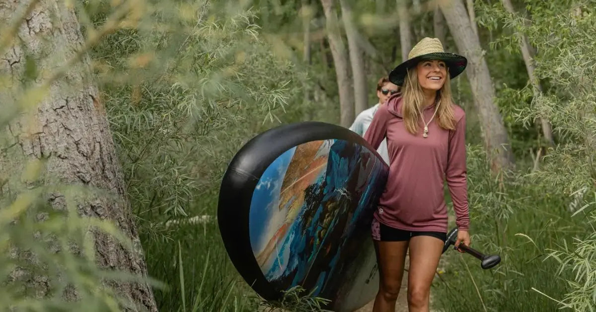 Woman carrying an inflatable paddle board on a forest trail
