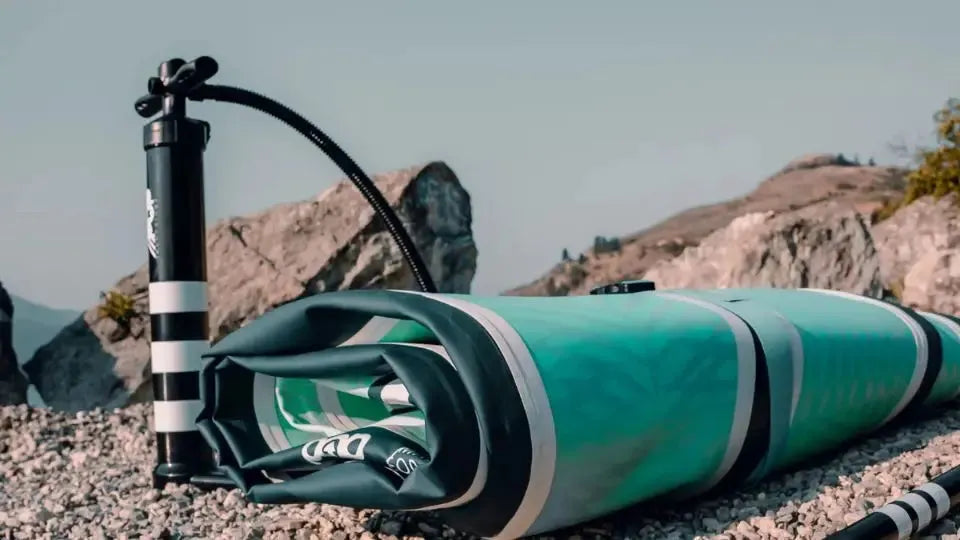 Folded inflatable paddle board with pump and paddle on rocky shore ready for storage