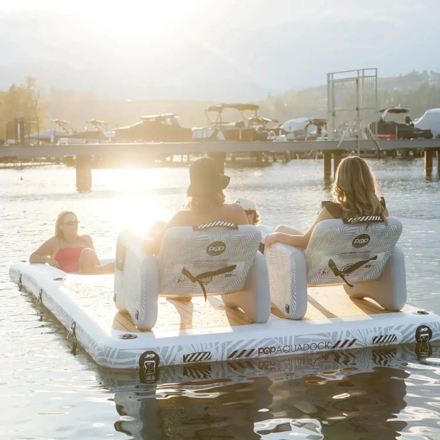 Friends lounging on an Aqua Dock inflatable platform with Inflateable chairs, enjoying a sunset by the marina.