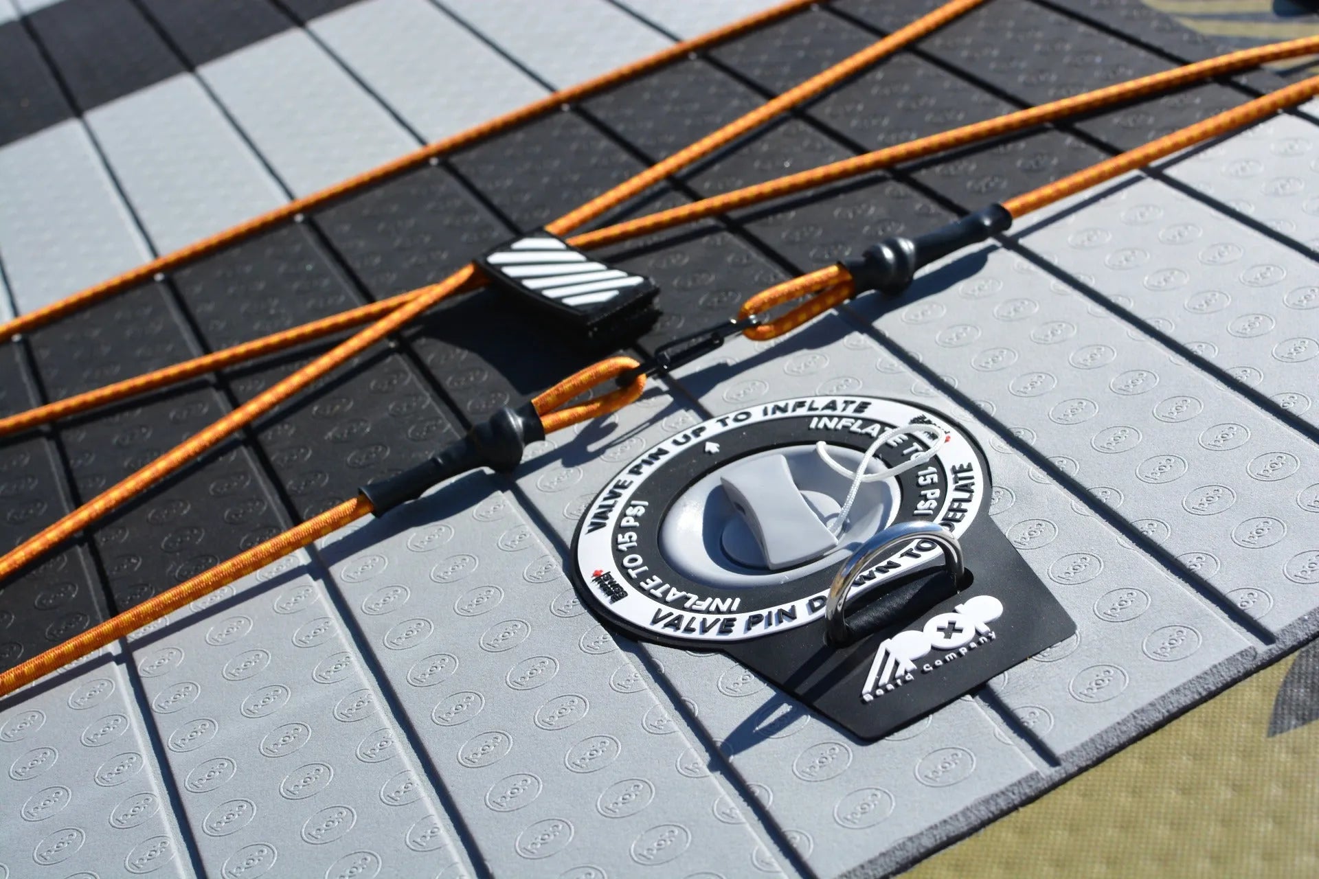 Close-up detail of the inflation valve and D-ring anchor point on the El Capitan Bomber paddleboard, showing the textured non-slip deck pad and orange cargo bungees.
