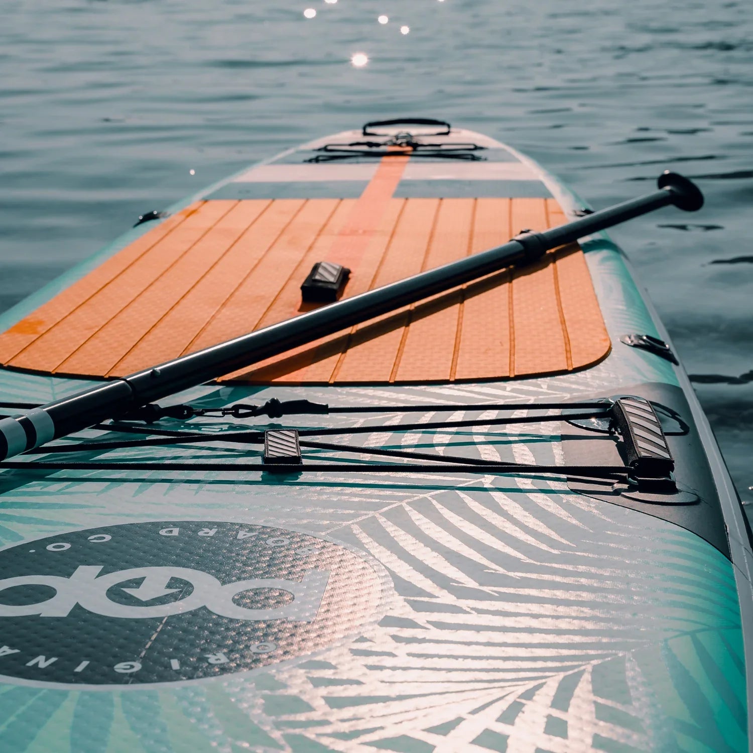 POP Yacht Hopper paddleboard on water showing paddle, orange traction pad, and bungee system.