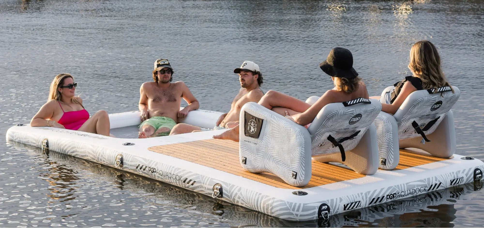 Group relaxing on POP AquaDock inflatable dock with chairs on the water.