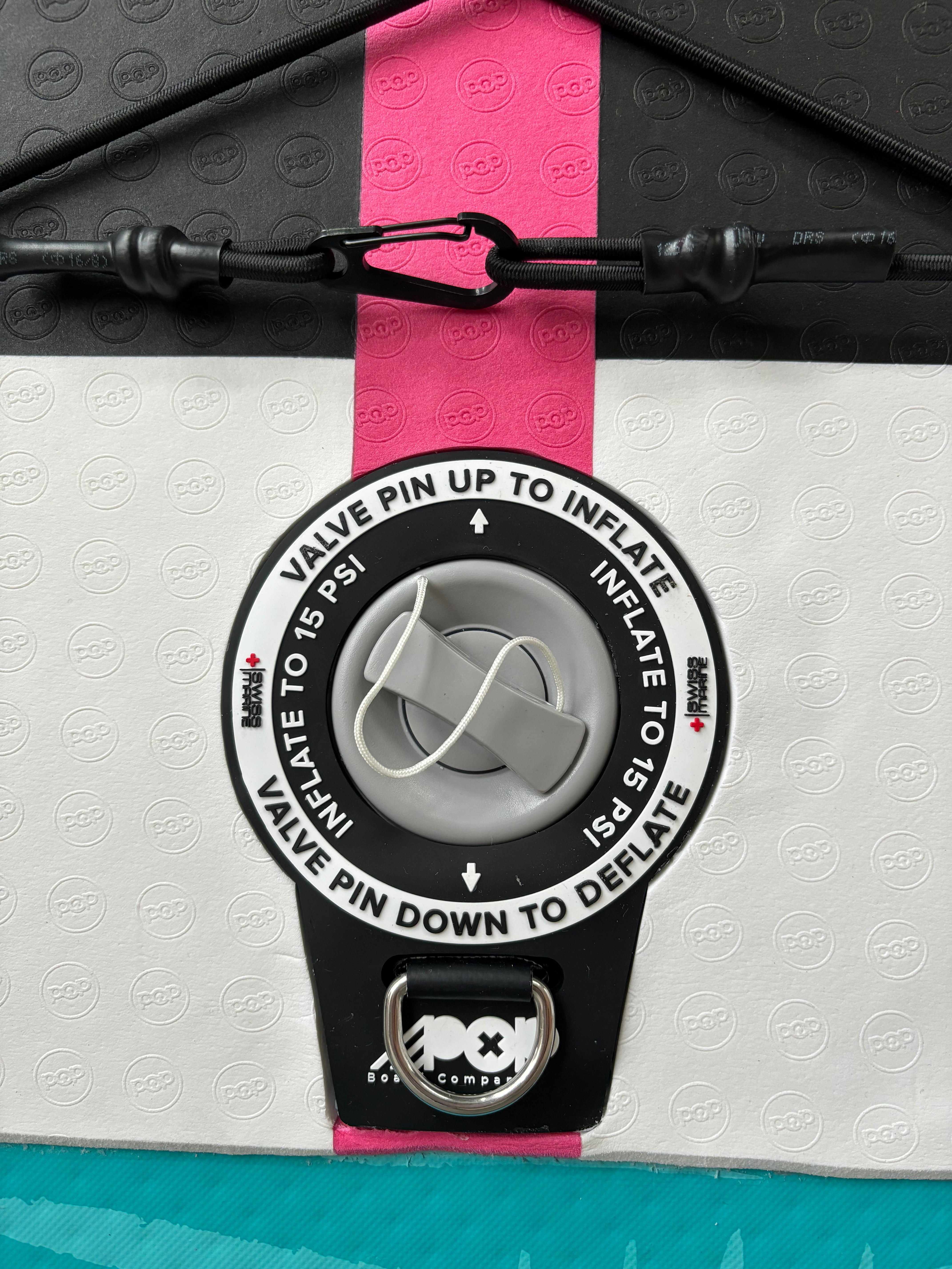 Close-up of the high-pressure inflation valve on the Yacht Hopper paddleboard, displaying "Inflate to 15 PSI" instructions on a white textured deck pad with a pink center stripe.